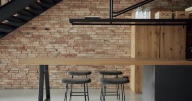 Modern and spacious wooden kitchen room with wall bricks and black staircase. Real Estate. Luxury kitchen with wooden island and chairs. Modern interior in luxury house. Minimalist design in New Home.