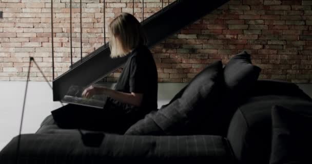 一个女人坐在黑色的沙发上看书 奢华的现代住宅与角落索法和书架 时尚的家具 简约家庭内部 舒适的现代家具设计 — 图库视频影像