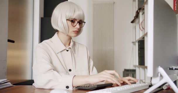 在台式电脑上工作的戴眼镜的年轻女性 年轻的女商人在自家办公室的电脑上工作 努力工作以确保她成功 在办公室内部工作的年轻女商人 — 图库视频影像