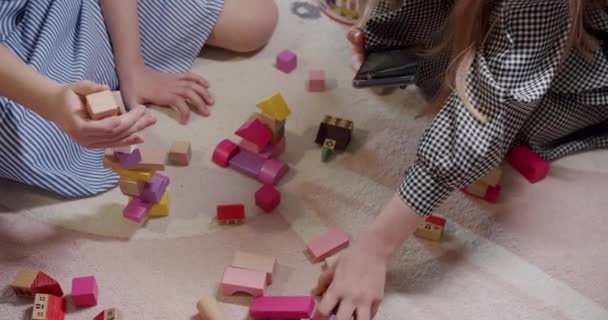 おもちゃで遊ぶ子供たちは自宅の床カーペットに座っています 子供たちは木のブロックの塔を建てる リビングルームでゲームをお楽しみください 木製の建物ブロックで遊ぶ子供 ゲームアクティビティを楽しむ — ストック動画