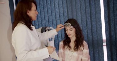 Oftalmolog kadın, klinik kabinesinde optometrist deney çerçevesi olan bir hastayı muayene ediyor. Profesyonel göz doktoru, genç bayan müşterinin görme yetisini arttırıyor..