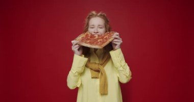Pepperoni pizza yiyen güzel aç kız, kırmızı izole edilmiş arka planda eğleniyor ve gülümsüyor. Pizza seven aç bir kadın. Lezzetli bir dilim Pepperoni pizzası yiyorum..