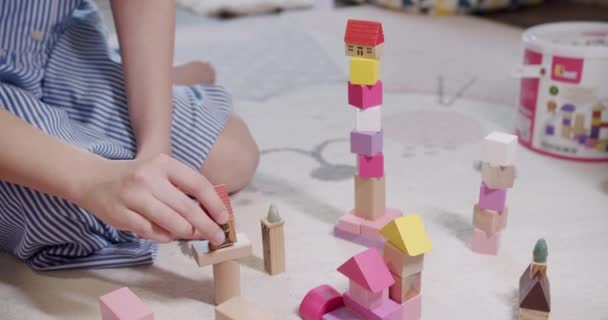 おもちゃで遊ぶ子供たちは自宅の床カーペットに座っています 子供たちは木のブロックの塔を建てる リビングルームでゲームをお楽しみください 木製の建物ブロックで遊ぶ子供 ゲームアクティビティを楽しむ — ストック動画