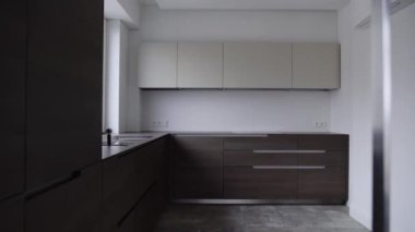 Modern iç mekanı olan şık bir mutfak, ahşap malzemeli kahverengi dolap, entegre ev aletleri ve musluk ile lavabo. Yeni mutfakta minimalist stil.