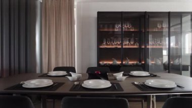 Modern apartmandaki yemek odasında minimalist tasarımı olan şık bir masa. Boş beyaz tabaklar ve gümüş çatal bıçak seti. Tahta masa üstünde siyah kaplar. Akşam yemeği konsepti