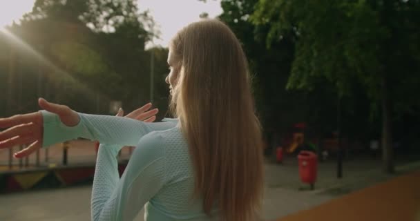 公園の屋外で運動する前に暖かくなる青いアクティブウェアの魅力的なスポーティな女の子のバックビュー 夏の朝 外で運動する若い女性 健康的なライフスタイルのコンセプト — ストック動画