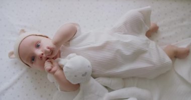 Bebek tulumlu şirin bir bebek ve kulakları beşikte uzanmış komik şapkalı, peluş tavşan oyuncağı çiğneyen ve bebek odasında kameraya bakan komik bir bebek..