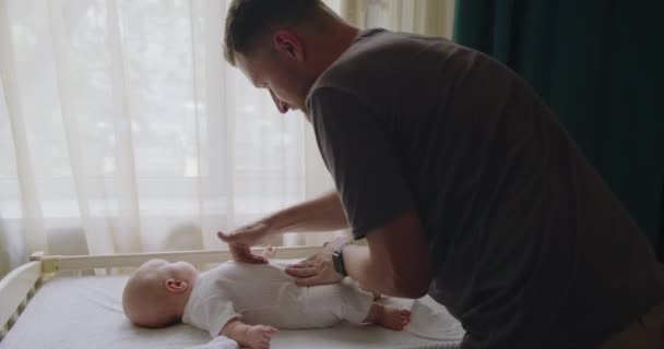 年轻男子父亲温文尔雅地按摩着可爱婴儿的腹部 放在更衣室的桌子上 爸爸花时间和新生儿在一起 照顾他 父母身份的概念 — 图库视频影像