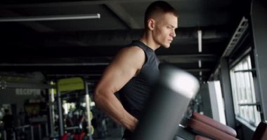 Antrenman aletleri üzerinde egzersiz yapan ve fitness kulübündeki kameralara bakan genç bir atletik. Kaslı sporcu adam modern spor salonunda çalışıyor. Sporcunun ciddi portresi