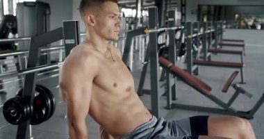Vücut kaslı, kaslı, spor salonundaki bankta oturan ve antrenmandan sonra dinlenen genç yakışıklı adama yan bakış. Tişörtsüz atletik erkek spor salonunda egzersiz yapmaya ara veriyor.