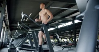 Sporcu adam spor salonunda egzersiz yapıyor ve koşu bandında koşuyor. Gömleksiz, kaslı vücutlu genç bir erkek spor kulübünde egzersiz yapıyor. Sağlıklı yaşam tarzı kavramı.