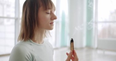 Palo Santo ile meditasyon yapan kadın, Bursera Graveolens kutsal ahşap, stüdyoda dinlenme zen uygulaması, bitkisel şifa, yoga veya aura temizliği. Esrarengiz ayinler için gerekli tütsü, 