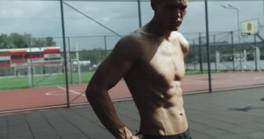 Kaslı vücudu ve mükemmel kasları olan kendine güvenen bir adam antrenmandan sonra spor sahasında duruyor. Atletik erkek dışarıda egzersiz yapıyor..