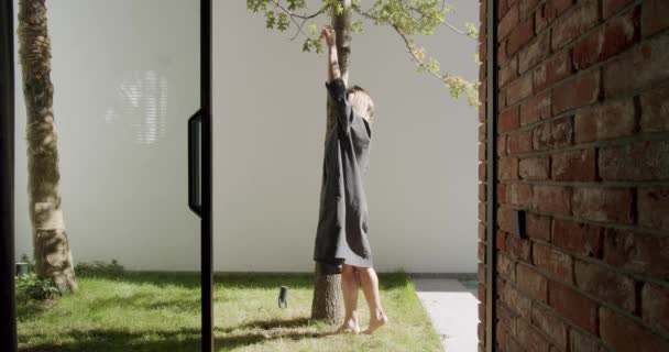 在阳光明媚的夏日 年轻女子在后院休息 触摸树木 赤脚在绿草上行走 自然联系概念 — 图库视频影像