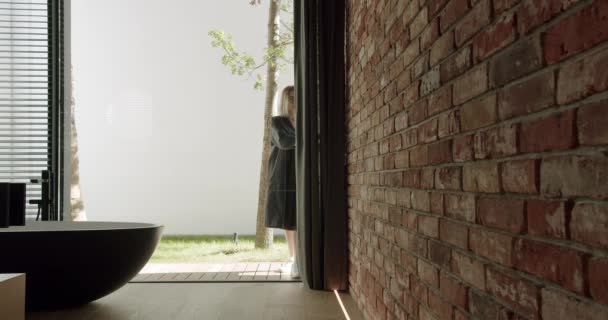妇女打开滑动式玻璃门 带着独立的浴缸 砖墙和现代阁楼进入村舍的房间 — 图库视频影像