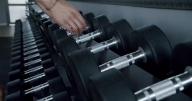 Erkek eli, spor salonunda çalışmak için askıdan demir halterler alır. Atletizm sporcusu, spor malzemeleriyle ağırlık antrenmanına hazırlanıyor.