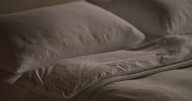 Rahat çift kişilik yatağa, beyaz yastıklara ve otel odasında ya da modern dairede pamuk kaplı yorgana yakın çekim. Yatak odasında buruşmuş tekstil yatağı. Sabah konsepti