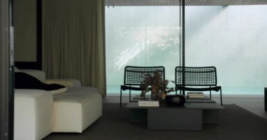 Konforlu kanepe, çiçekli vazo kahve masasında kitaplar, örülmüş koltuklar ve sürgülü cam kapılar..