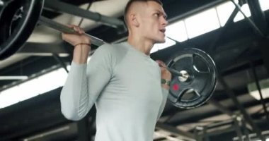 Genç atletik adam spor salonunda ağır demir halterleri kaldırıyor. Güçlü erkek fitness kulübünde spor malzemeleriyle antrenman yapıyor.