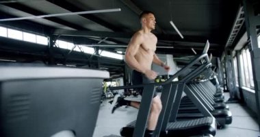 Modern spor salonunda koşu bandında koşan genç bir atletik. Sportif gömleksiz, kaslı vücutlu bir erkek spor kulübünde spor aletleriyle antrenman yapıyor. Etkin yaşam biçimi