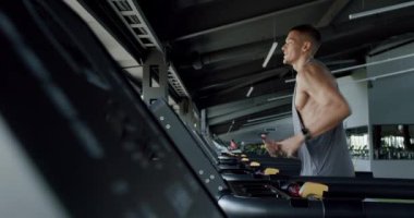Modern spor salonunda egzersiz yapan ve koşu bandında koşan kaslı adama yan bakış. Spor giyimli genç adam spor salonunda kardiyo çalışması yapıyor. Etkin yaşam tarzı kavramı