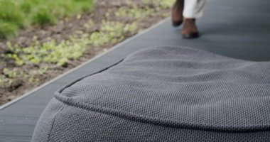 Terastaki koltuk koltuğuna ve arka planda yürüyen insan bacaklarına odaklan. Dışarıdaki çerçevesiz sandalyenin gri döşeme kumaşına yakın.. 