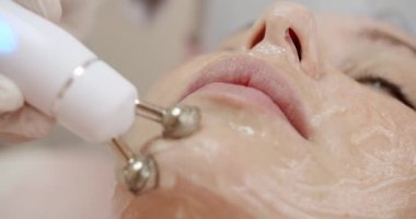 Güzellik kliniğindeki kadın müşteriler için modern aletler kullanarak yüz mikro akımı prosedürü yapan profesyonel kozmetikçilere yakın çekim. Kozmetik ve cilt bakımı kavramı