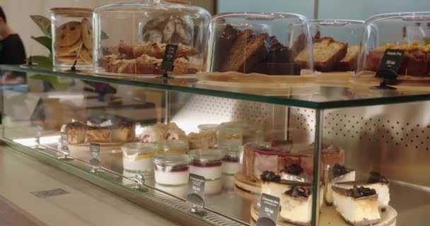 カフェのガラスショーケースで さまざまな甘いデザート ケーキ 新鮮なペストリーのクローズアップ 店舗での菓子の品揃えによる表示 — ストック動画