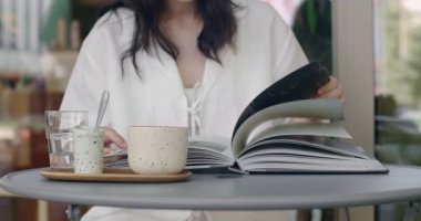 Kafede, açık havada kahve içen, kitap okuyan, sayfaları çeviren ve yaz günü dinlenen genç bir kadın.. 