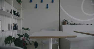 Kafenin modern iç kısımları hafif tonlarda, sandalyeli ahşap masa, çaydanlıkta yeşil bitki ve raflarda kahve paketleri..