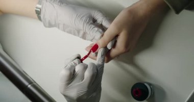 Manikür ustası ellerin üst görüntüsü. Güzellik salonunda müşteri tırnağına kırmızı jöle sürerken. Kadın elleri için profesyonel bakım
