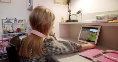 7 yaşındaki kız, çocuk odasında pembe kulaklıklarla oynuyor ve dijital tablet kullanıyor, sosyal ağdaki havalı video veya fotoğraf içeriğinin tadını çıkarıyor, çevrimiçi oyunlar oynuyor..