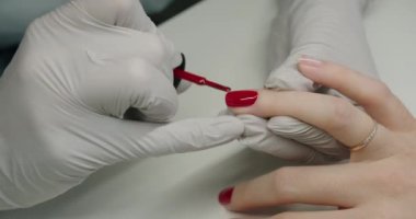 Manikür ustası eldiven giymiş müşterinin tırnaklarını güzellik salonunda kırmızı jel cilasıyla kaplayan ellerin yakın çekimi. Kadın elleri için profesyonel bakım