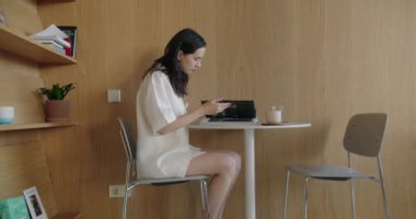 Kafe masasında oturan genç bir kadın kahvaltı sırasında latteyle kitap okuyor. Modern iç mekanlı bir kafede dinlenirken kadın öğrenci dergi sayfalarını çeviriyor.