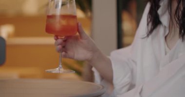 Restoranda oturmuş, buzlu ve buzlu soğuk kokteyl içen bir kadın. Alkollü içeceği meyve suyuyla deneyen ve kafede dinlenen bir kadın..