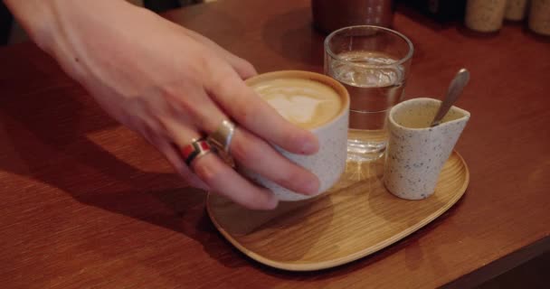 バリスタのクロップビューでは ホットラテとサーバーハンドを用意し コーヒーショップでクライアントに竹のトレイで飲みながらカップを取ります カフェでセラミックマグでカプチーノを提供するクローズアップ — ストック動画