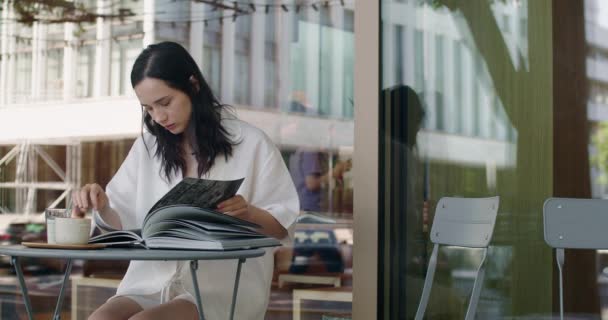 Ελκυστική Νεαρή Γυναίκα Διαβάζει Βιβλίο Ενώ Κάθεται Στο Τραπέζι Καφέ — Αρχείο Βίντεο