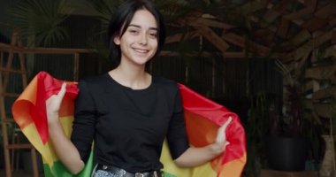 Lgbtq konsepti. Neşeli güzel kız elinde gökkuşağı çizgili bayrak, lgbt sosyal hareketinin sembolü. Genç esmer lezbiyen kadın gülümseyip kameraya bakıyor..
