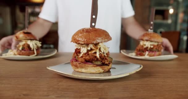 パブのクライアントのためのプレートに新鮮なハンバーガーを提供する男性ウェイターのクロップビュー バーの木のテーブルの美味しいハンバーガーのクローズアップ 男は夕食のために顧客にチーズバーガーを持って来ます — ストック動画