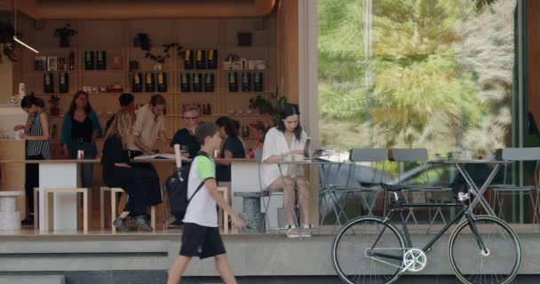 シナウ モルドバ 人々は 居心地の良いストリート カフェで休息し 人々は街を歩き 車を通り過ぎます 屋外のテーブルに座っている女性は 本を読んでコーヒーを飲む 都市ライフスタイル — ストック動画
