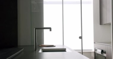 Mutfakta modern tarzda detaylar, paslanmaz çelik musluk, ev aletleri, modern mobilyalar ve cam sürgülü kapı ayırma odası. Minimalist tasarımı olan bir daire