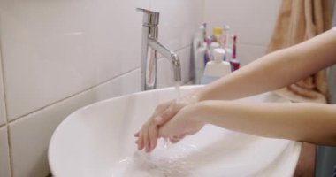 Elleri lavaboda muslukla yıkayan çocuk manzarası. Çocuk banyoda elleri temizlemek için sabun ve akan su kullanıyor. Günlük hijyen rutini. Sağlık ve hastalık önleme