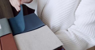 Kadın eli kataloğu kumaş örnekleriyle kapalı tutuyor ve iç dekorasyon için renk seçiyor. Kadın tasarımcının kırpılmış görüntüsü perde ya da mobilya için tekstil seçiyor. İçerde gelişme var.