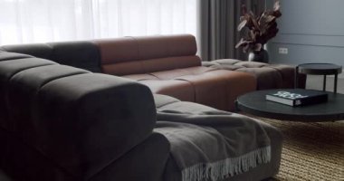 Modern iç mekanı olan şık bir oturma odası, ekoseli rahat bir kanepe, halı üzerinde yuvarlak bir sehpa, bitki ve perdeli bir vazo. Çağdaş tasarımı ve mobilyası olan lüks bir daire.