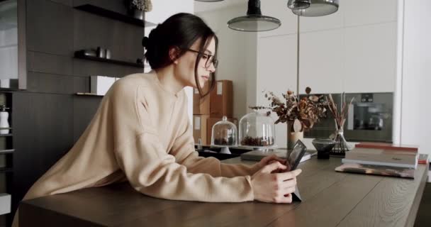 戴着眼镜的年轻漂亮的女人在家里用平板电脑上网购物 现代公寓平板电脑网站上的Brunette女性搜索信息 — 图库视频影像