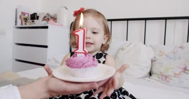 Doğum gününü kutlayan güzel bir kız bebek, kekin üzerine mum üfleme ve çocuk odasında yatakta otururken el çırpma heyecanı. Mutlu bebek evde ailesiyle bir yıl kutluyor..