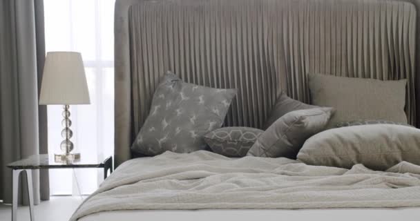 덮개를 부드러운 담요와 베개와 편안한 침대가있는 침실의 현대적인 인테리어 램프와 — 비디오