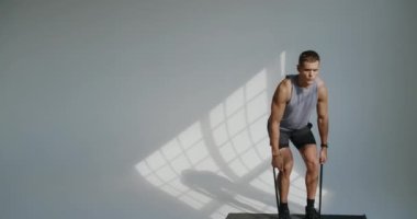 Genç atletik adam egzersiz yapıyor ve stüdyoda beyaz arka planda direnç bandı kullanarak kaldırma egzersizi yapıyor. Spor malzemeleriyle egzersiz yapan kaslı bir adam..
