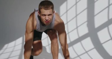 Atletik adam spor yapar ve beyaz arka planlı stüdyoda egzersiz yapmak için dambılları alır. Genç erkek vücut geliştirici pazı eğitimi için spor malzemesi kullanıyor. Fitness konsepti