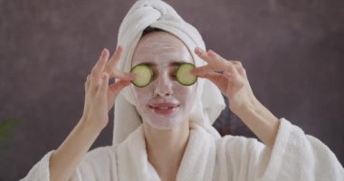 Kafasında havluyla gözlerini salatalıkla kaplayan bornozlu, neşeli, genç bir kadın taze, sağlıklı cilt bakımı konsepti sunuyor. Bath 'dan sonra, kadınlar için Spa güzellik prosedürleri.